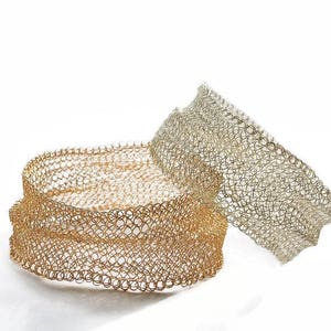 May include: Two wire mesh bracelets. One is gold-toned, and the other is silver-toned. The bracelets are made of small, interconnected circles, creating a flexible, open weave design. The gold bracelet is stacked, while the silver one is angled.
