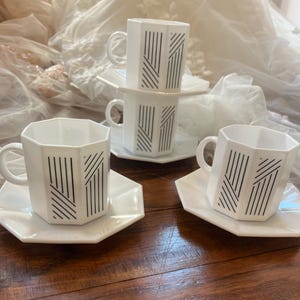 May include: Set of four white ceramic coffee cups with matching saucers. The cups and saucers have a geometric black and white design.
