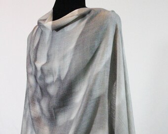 Puede incluir: Un chal de pashmina gris y blanco con una textura suave y fluida. El chal está drapeado sobre un maniquí y tiene un patrón abstracto sutil.