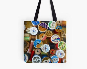Pode incluir: Uma bolsa tote com um padrão colorido de carretéis de fio. Os carretéis são de várias cores, incluindo vermelho, azul, verde, amarelo e marrom. Os carretéis estão dispostos em um padrão aleatório, criando um design visualmente atraente.