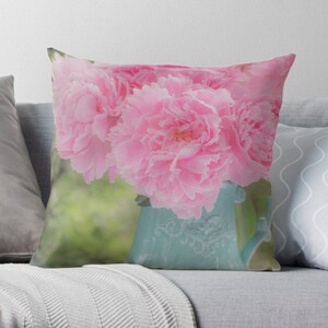 May include: A bouquet of pink peonies in a light blue ceramic pitcher with a floral design. The peonies are in full bloom and have a soft, delicate appearance.
