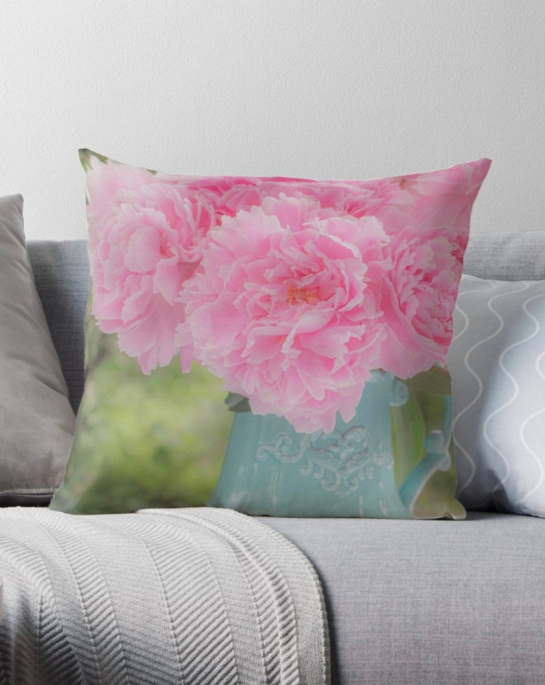 May include: A bouquet of pink peonies in a light blue ceramic pitcher with a floral design. The peonies are in full bloom and have a soft, delicate appearance.