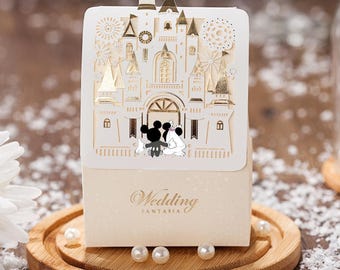Puede incluir: Una caja de regalo de boda blanca con un diseño de castillo dorado y las figuras de Mickey y Minnie Mouse. La caja dice "Wedding Fantasia" en la parte delantera.