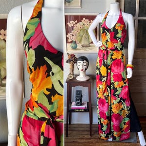 Könnte beinhalten: Ein Neckholder-Jumpsuit mit einem lebendigen Blumenmuster in Rot-, Rosa-, Orange-, Gelb- und Grüntönen auf schwarzem Hintergrund. Der Jumpsuit hat eine Bindetaille und ein weites Bein, präsentiert auf einer Schaufensterpuppe.