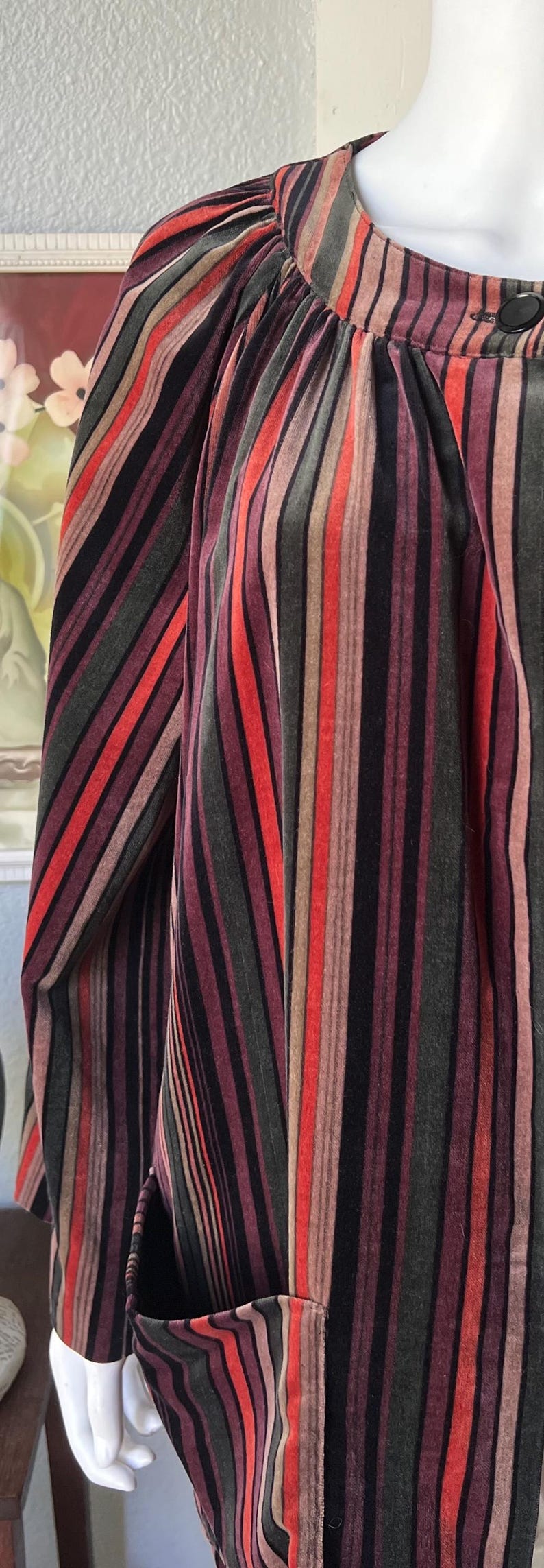 May include: A velvet garment with vertical stripes in shades of red, black, brown, and green. The garment has a high neckline and a button closure. The sleeves are long and the overall style is vintage.