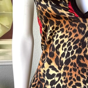 May include: A sleeveless dress with a leopard print pattern in shades of brown and black. The dress features red rose accents and a black trim. The garment is displayed on a mannequin.