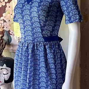 May include: A blue and white short-sleeved dress with a turtle print. The dress has a v-neck and a tie at the waist.