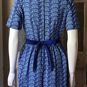 May include: A blue short-sleeved dress with a white turtle print. The dress has a navy blue sash that ties at the back.