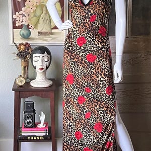 May include: A leopard print dress with red rose accents. The dress features a keyhole neckline and a high side slit. The dress is displayed on a mannequin.