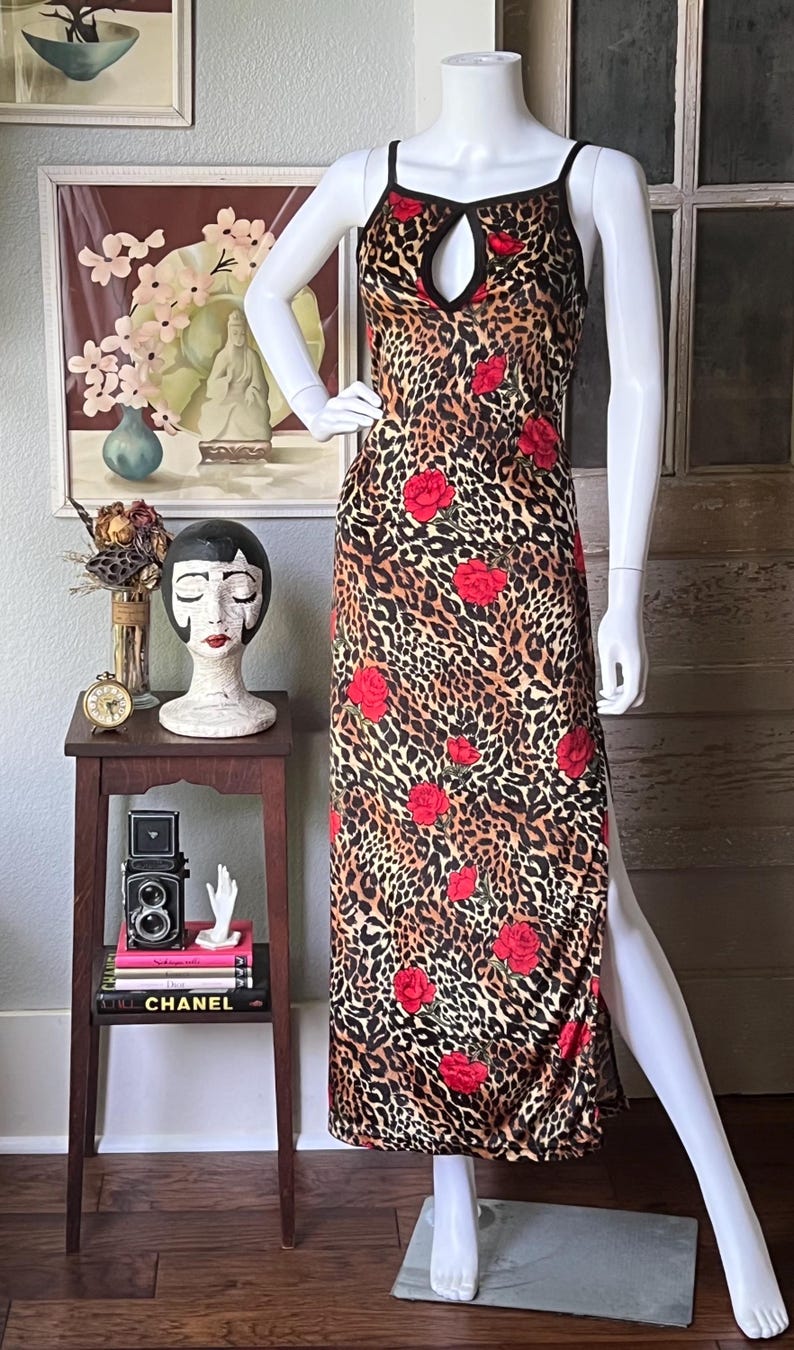May include: A leopard print dress with red rose accents. The dress features a keyhole neckline and a high side slit. The dress is displayed on a mannequin.