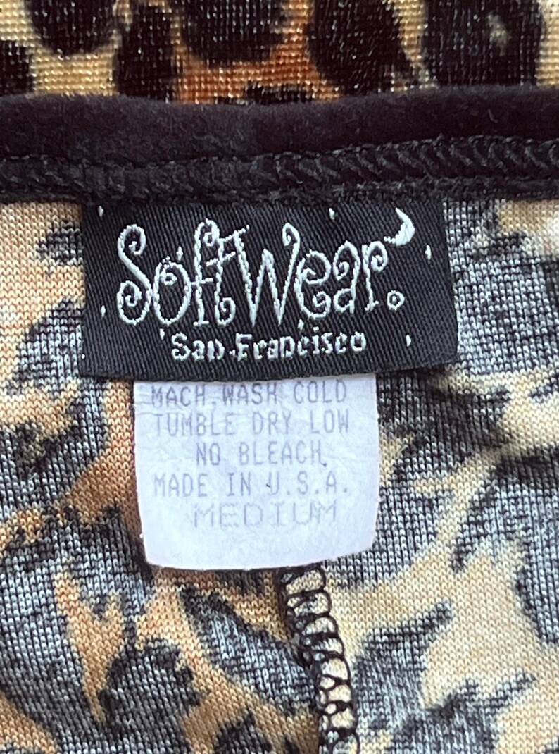 May include: Close-up of a garment with a leopard print pattern. A black label reads "SoftWear, San Francisco." A smaller tag indicates care instructions: "MACH WASH COLD, TUMBLE DRY LOW, NO BLEACH, MADE IN U.S.A., MEDIUM."