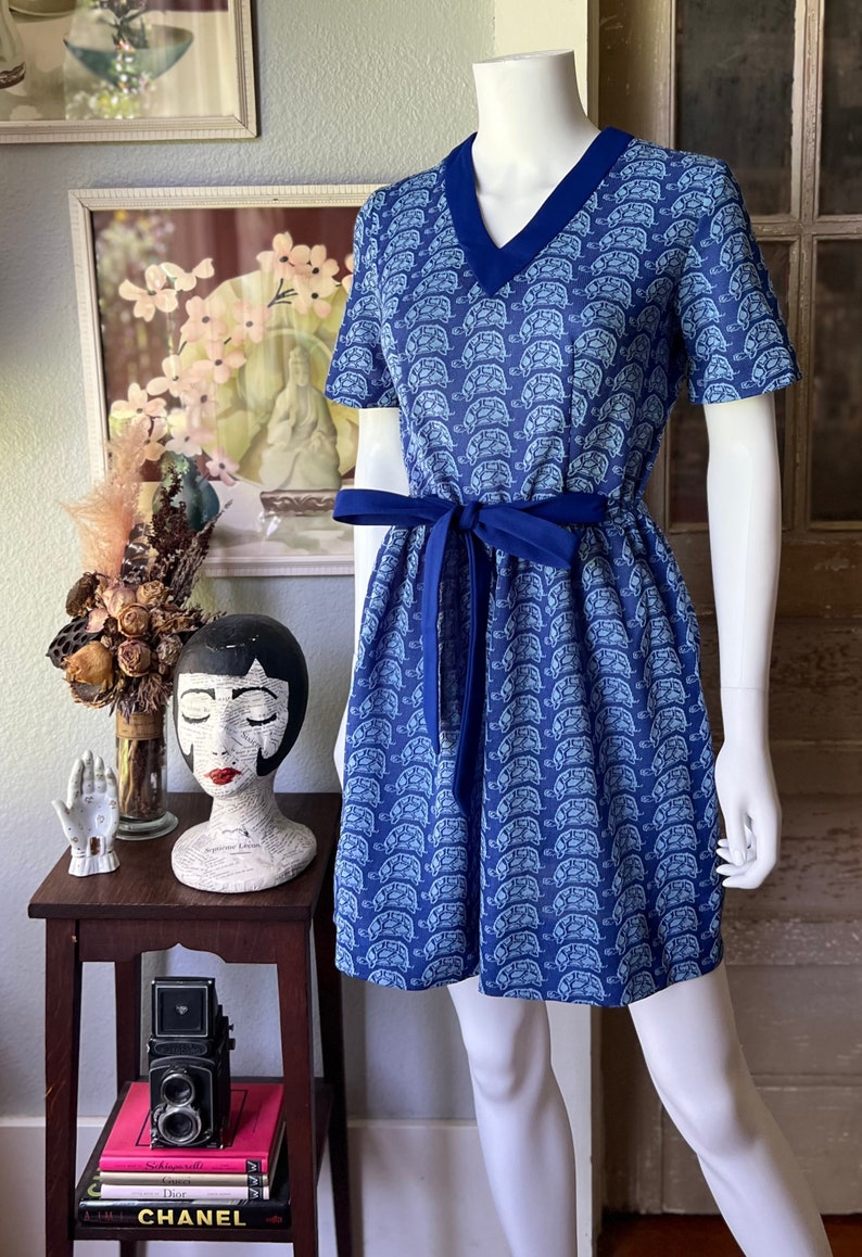 May include: A blue and white short-sleeved dress with a turtle print and a blue sash tie.