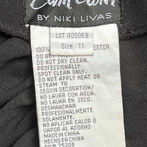 以下が含まれることがあります： Zum Zum by Niki Livas の衣料品の洗濯表示が書かれた白いタグ。タグには、「100% エステル」、「LOT IF05069」、「サイズ 11」、「ドライクリーニング不可」、「ドライクリーニングは専門店へ」、「ビーズ装飾には熱や蒸気を当てないでください」、「水洗い不可」、「ドライクリーニング不可」、「ドライクリーニングは専門店へ」、「装飾には熱や蒸気を当てないでください」、「中国製」、「HECHO EN CHINA」、「RN# 75308」、「STYLE# 9356」、「LOT# IF05069」と記載されています。