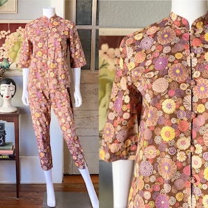 May include: A brown and pink floral print pyjama set with a mandarin collar and long sleeves. The trousers are cropped and the top has a button closure.