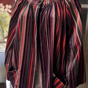 May include: A multi-colored striped jacket with a round neckline and two front pockets. The jacket features vertical stripes in shades of red, green, black, and brown. The garment is displayed on a mannequin.