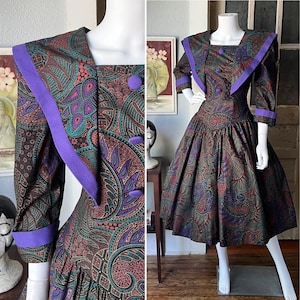 Może przedstawiać: Sukienka w stylu vintage z wzorem paisley w odcieniach brązu, turkusu i fioletu. Sukienka ma kwadratowy dekolt, rękawy trzy czwarte i pełną spódnicę. Kołnierz i mankiety są wykończone żywym fioletem.