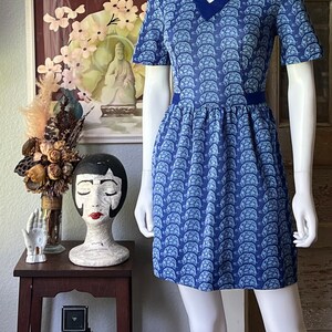May include: A blue and white short-sleeved dress with a v-neck and a pattern of white turtles on a blue background. The dress has a blue trim around the neckline and waist.
