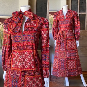 Puede incluir: Un vestido rojo y azul con estampado de manga larga y un lazo en el cuello. El vestido tiene un patrón geométrico con un diseño de paisley.