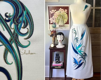 May include: White skirt with a blue, teal, and gold abstract floral design. The skirt is displayed on a mannequin. The word "Shaheen" is embroidered on the fabric. The skirt is a vintage item.