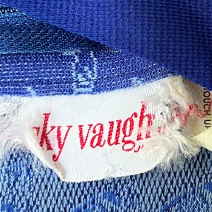 May include: A white tag with red text that reads "ky vaughn" attached to a blue fabric.