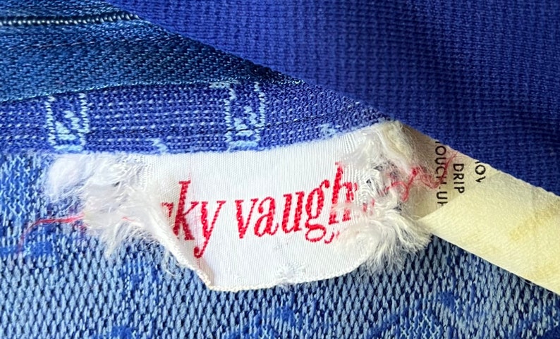 May include: A white tag with red text that reads "ky vaughn" attached to a blue fabric.
