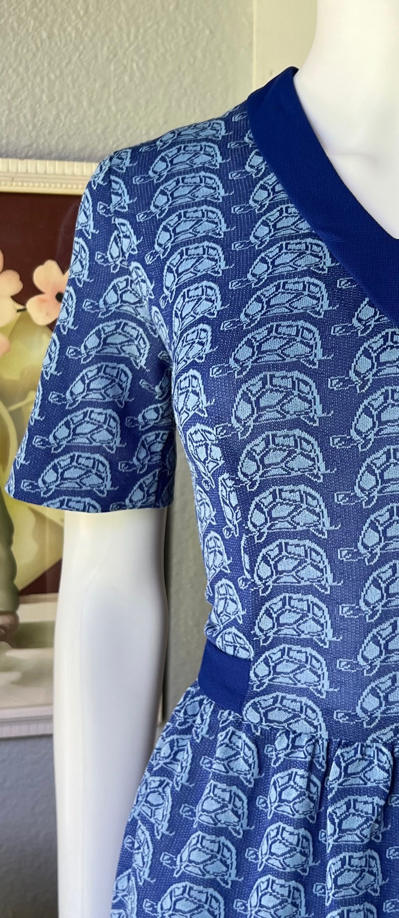 May include: A blue and white short-sleeved dress with a turtle pattern. The dress has a blue collar and a blue waistband.