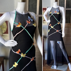 May include: Black halter dress adorned with colourful butterfly appliqués and crisscrossing pastel ribbons. The dress has a sheer overlay and a floor-length skirt, creating an elegant and whimsical look. The butterflies are in shades of orange, yellow, and blue.