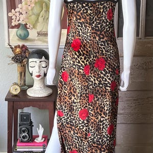May include: A leopard print dress with red rose accents. The dress has a black trim and spaghetti straps. The dress is displayed on a mannequin. The dress has a slit on the left side.