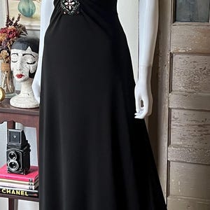 以下が含まれることがあります： ビーズがあしらわれた黒いホルターネックのロングドレス。ドレスは体にフィットしたボディと、ゆったりとしたスカートが特徴です。