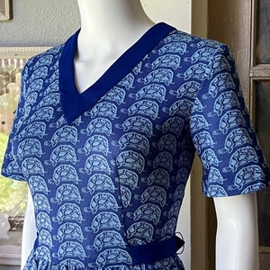 May include: A blue dress with a white turtle pattern and a navy blue collar. The dress has short sleeves and a fitted bodice.