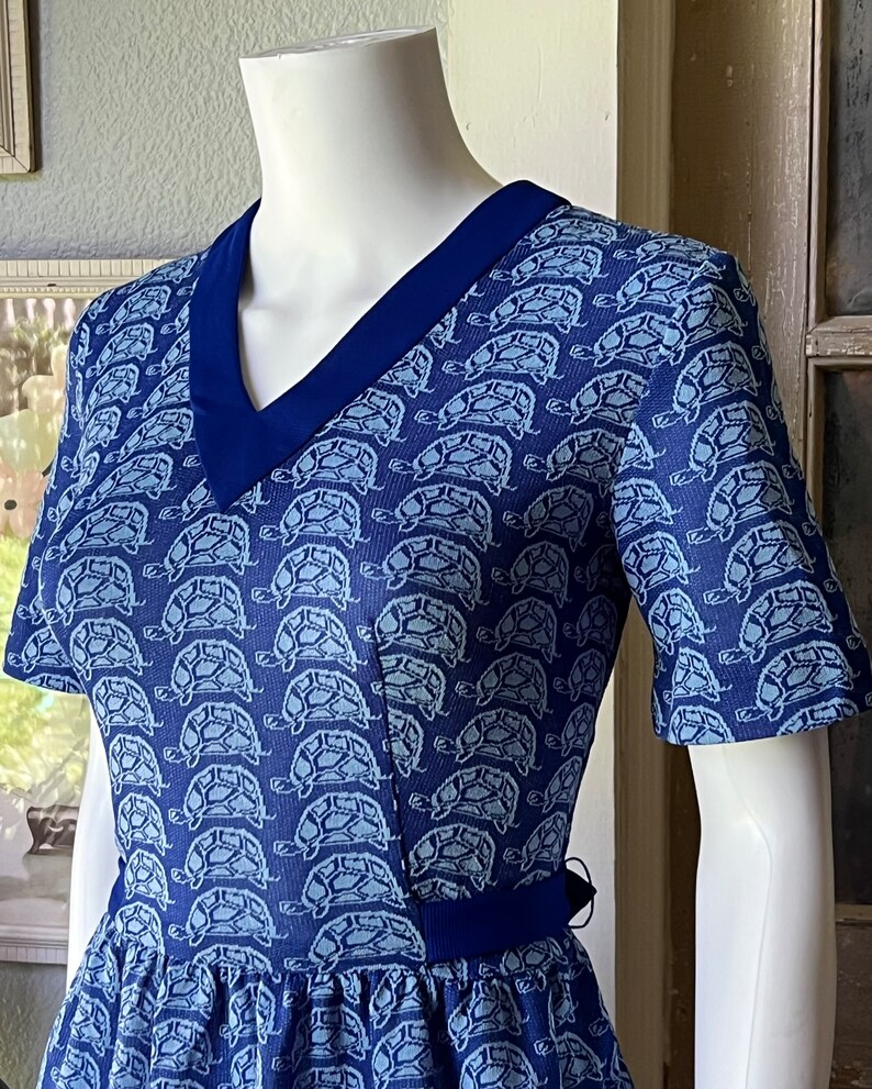 May include: A blue dress with a white turtle pattern and a navy blue collar. The dress has short sleeves and a fitted bodice.