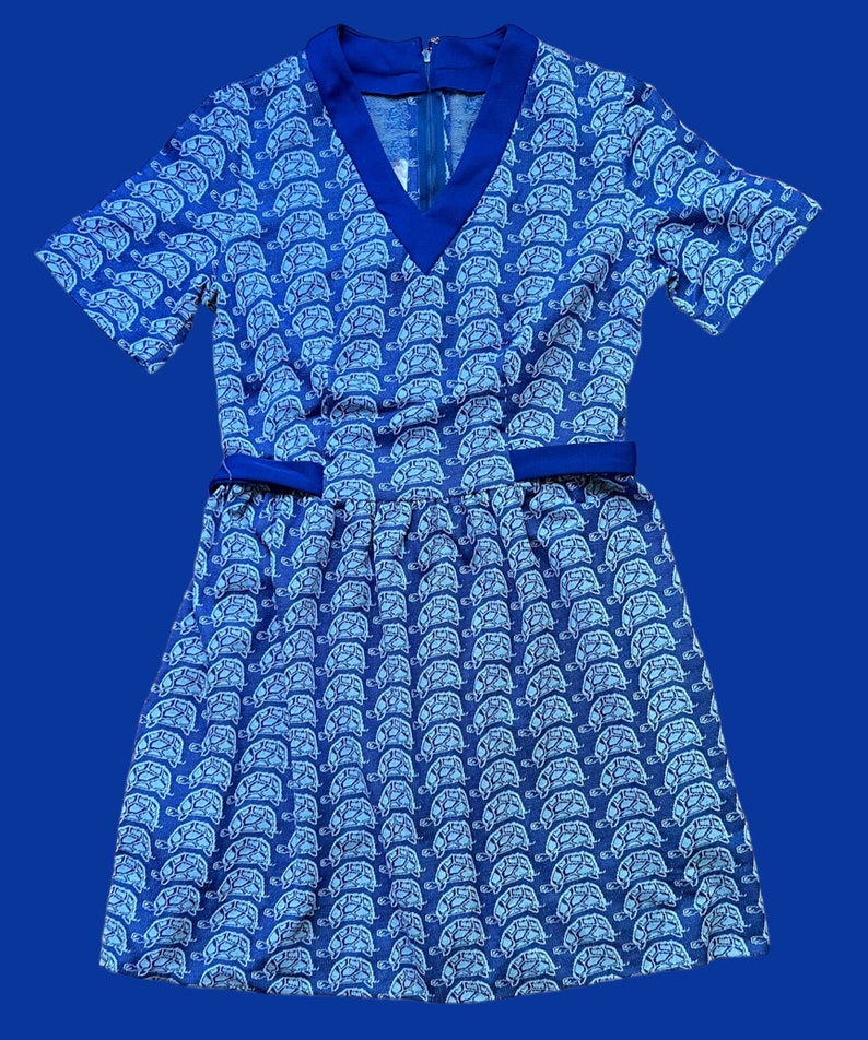 May include: A blue and white short-sleeved dress with a v-neck and a pattern of white turtles on a blue background.