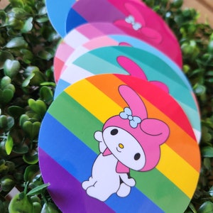 May include: A set of four round stickers featuring a rainbow, a teal and white striped design, a purple and white striped design, and a blue and white striped design. Each sticker features a cartoon character with a pink bow.