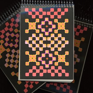 May include: A stack of spiral bound notebooks with a black cover and a geometric pattern in shades of pink, orange, and yellow. The pattern is symmetrical and features a repeating design of squares and diamonds.