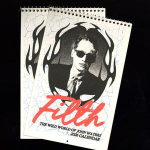 May include: Two spiral-bound calendars featuring a black and white portrait of a person wearing sunglasses, surrounded by a flame design. The word "Filth" is in red script, with the text "The Wild World of John Waters 2026 Calendar" below.