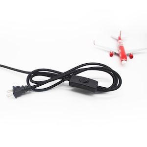 May include: Black electrical cord with a two-prong plug and an inline on/off switch. A red and white toy airplane is in the background.
