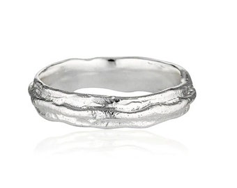 May include: A silver ring with a textured, organic design. The ring has a wide band with a rough, uneven surface.