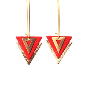 Peut inclure: Paire de boucles d'oreilles géométriques. Chaque boucle présente un triangle rouge superposé à un triangle doré et un triangle doré texturé. Elles sont suspendues à des crochets d'oreilles dorés. Design moderne et minimaliste.