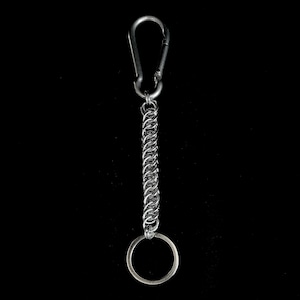 May include: A silver keychain featuring a carabiner clip and a chainmail-style chain. The chain leads to a small, circular key ring. The background is a plain black.