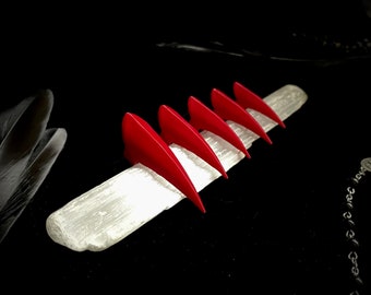 May include: Six red, pointed, claw-like shapes arranged in a row on a white, textured surface. The surface is on a black background.