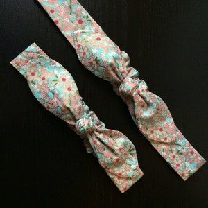 May include: Two blue headbands with a floral pattern in pink and white. The headbands are tied in a bow.