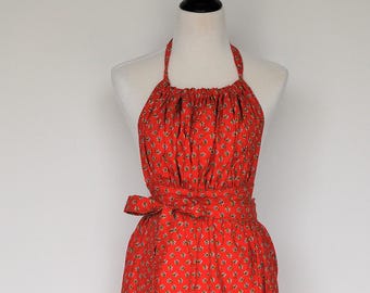 May include: A red apron with a white floral pattern and a tie at the waist. The apron is on a black mannequin stand.