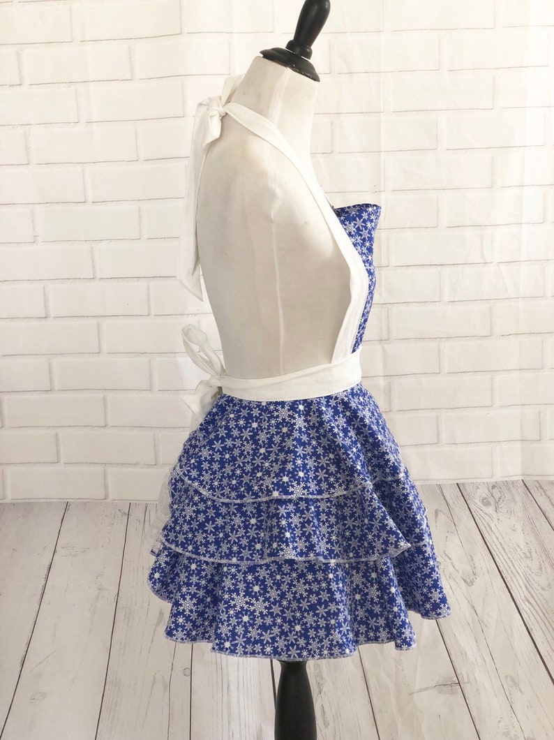 May include: A blue and white apron with a snowflake pattern. The apron has a white halter strap and a ruffled skirt.