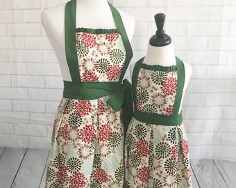 May include: Two green and white floral print aprons with green ribbon ties. The aprons are on mannequins.