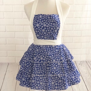 May include: A blue and white snowflake print apron with a white halter strap and a ruffled skirt.