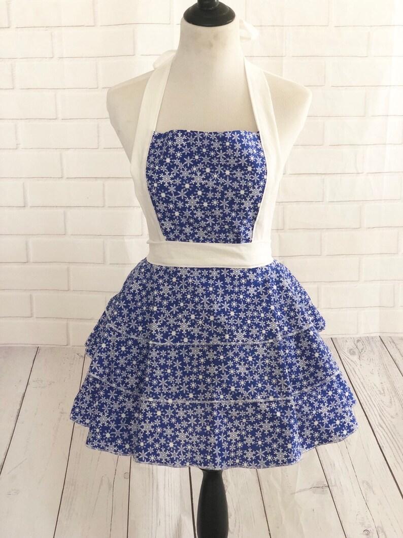 May include: A blue and white snowflake print apron with a white halter strap and a ruffled skirt.