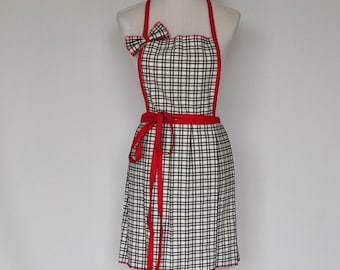 May include: A black and white checkered apron with red trim and a red bow. The apron has a long tie that wraps around the waist.
