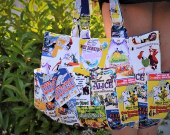 May include: A white tote bag with a colorful patchwork design featuring vintage Disney movie posters. The posters include titles like "Dumbo", "Snow White", "Alice in Wonderland", "The Jungle Book", and "One Hundred and One Dalmatians".