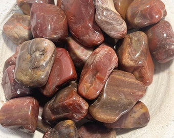 May include: A collection of tumbled red and brown jasper stones. The stones are smooth and polished, with a variety of patterns and textures.
