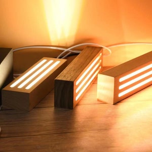 Puede incluir: Tres l&aacute;mparas rectangulares de madera con una luz blanca c&aacute;lida que emana de tres finas ranuras en cada l&aacute;mpara.